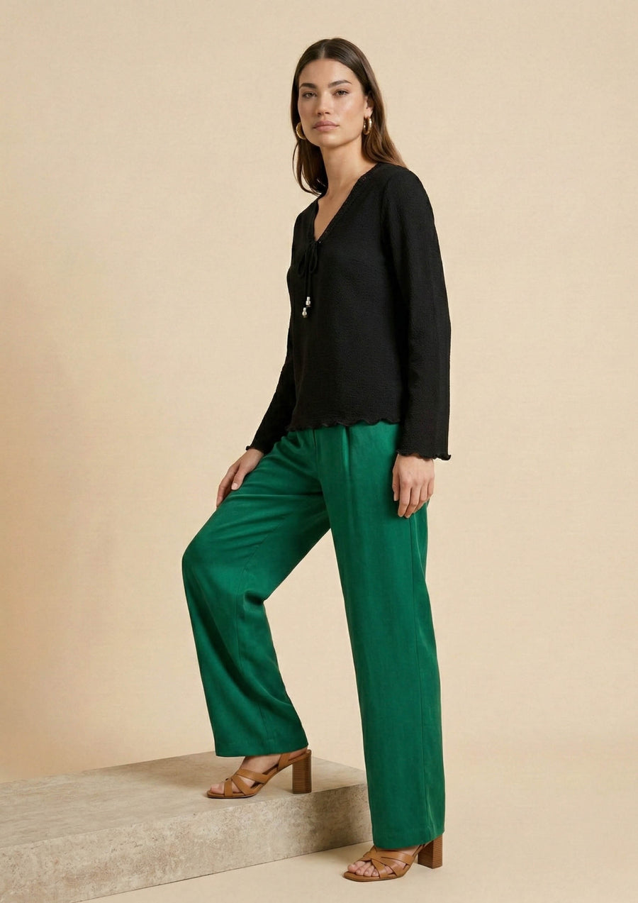 Model in Bewegung trägt die schwarze Bluse 'Duria'. Die locker fallende Silhouette (Loose Fit) bietet mühelose Eleganz für den Transit zwischen Business und Freizeit.