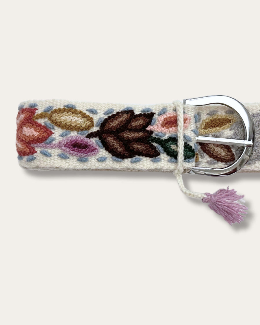 Gürtel Azulina von Ayni Ppacha, Nahaufnahme an der Schnalle: naturweiße Schafwolle, handbestickt mit Blättern in Rost, Braun, Violett, Blau und Grün, silberfarbene D-Schnalle mit Quaste