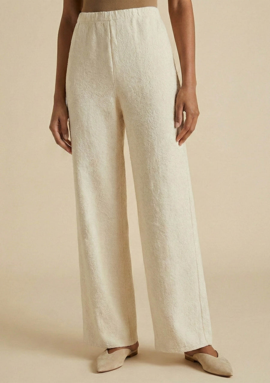 Model trägt die beige Hose 'Pradera' von Ayni Ppacha aus 100% ungefärbter Baumwolle. Die High-Waist-Hose im Straight-Leg-Schnitt besticht durch ein gerade geschnittenes Bein und eine natürliche Webtextur mit eingewebten Nazca-Symbolen als Details.