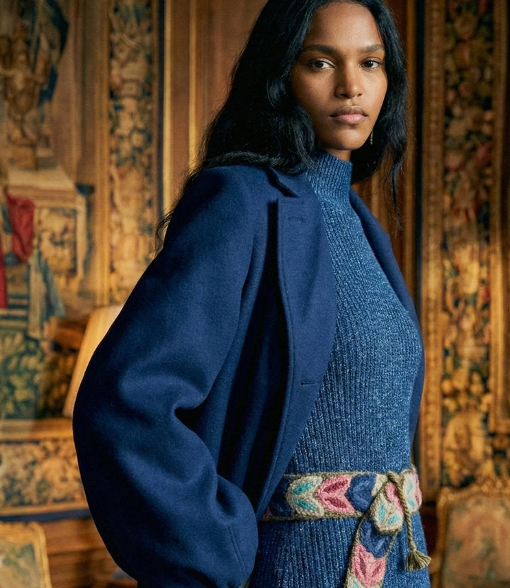 Frau in dunkelblauem Mantel und blauem Strickkleid, an der Taille der handbestickte Gürtel Morera von Ayni Ppacha mit Blattbögen in Koralle, Rosa und Hellblau