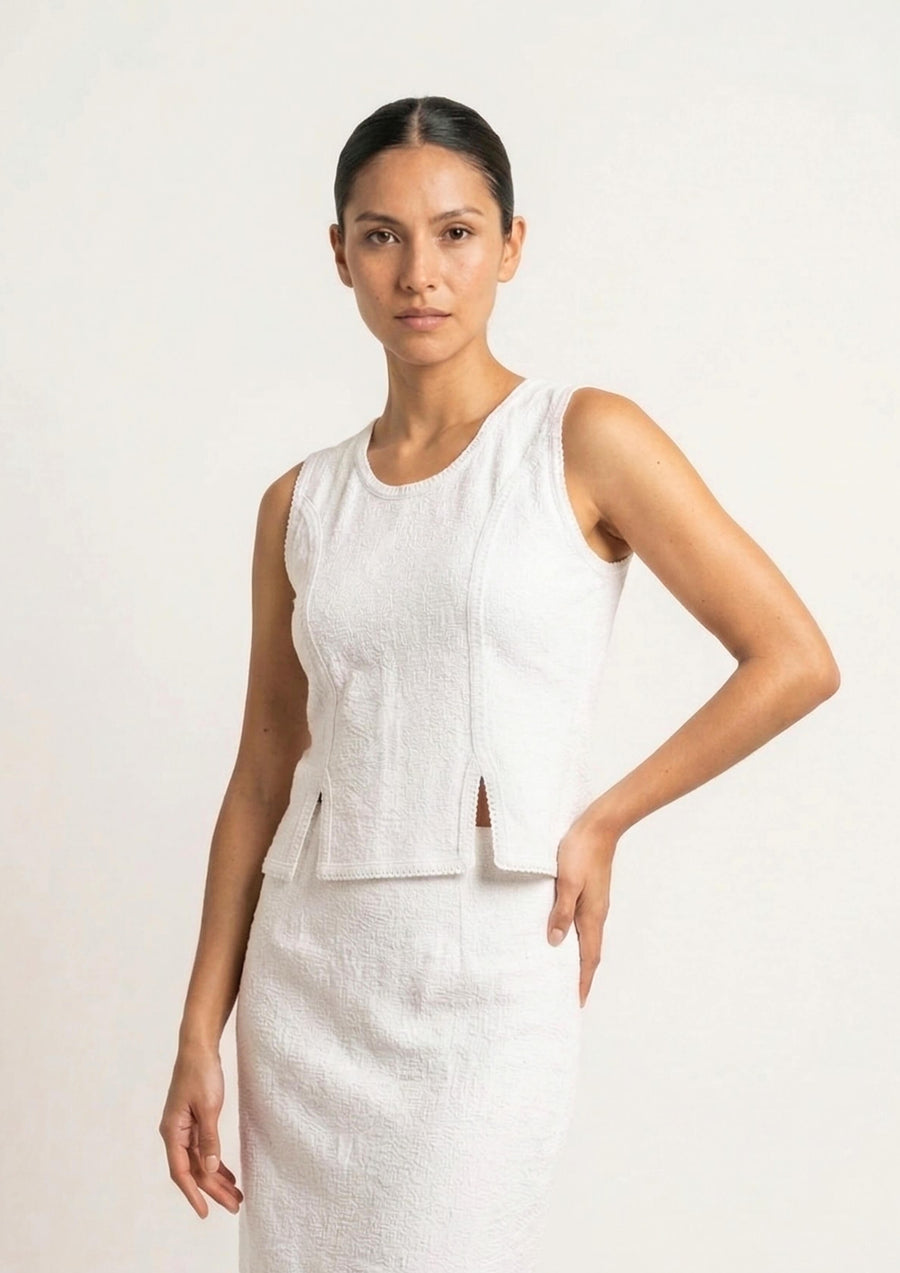Das weiße Tanktop 'Baila' von Ayni Ppacha aus strukturiertem Nazca-Baumwollwebstoff. Die Aufnahme zeigt die puristische Silhouette mit den charakteristischen Seitenschlitzen und der filigranen Häkelkante.