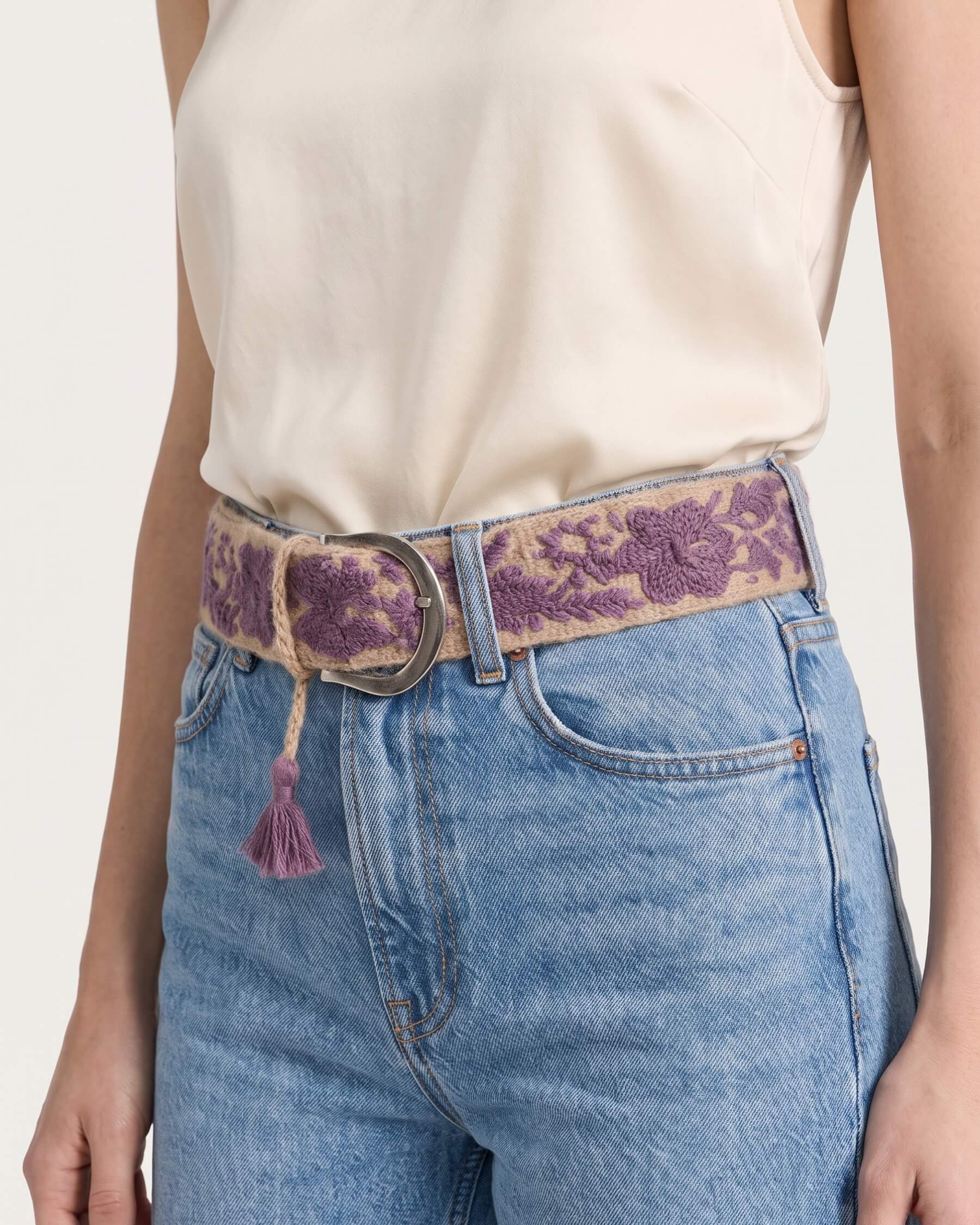 Detailaufnahme der Stickerei und Metallschnalle des handbestickten Ayni Ppacha Gürtels 'Violeta' aus 100% Schafwolle, in Rosa/Lila/Beige.