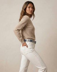 Profilansicht des handbestickten Gürtels 'Abelia' von Ayni Ppacha. Die Aufnahme betont die haptische Tiefe der blauen Blattstickerei auf naturweißer Schafwolle, getragen zu einem beigen V-Neck-Pullover und weißer High-Waist-Denim.