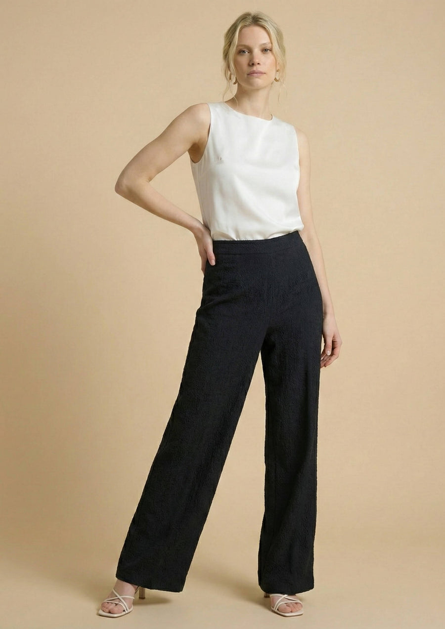 Frontale Ansicht der schwarzen Hose 'Pradera' kombiniert mit einem weißen Seidentop. Ein zeitloser Look, der die zarte Baumwollstruktur des Nazca-Baumwollwebstoffs hervorhebt.