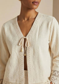 Detailaufnahme des zarten Bindebands am Cardigan 'Garbo', die die feine Webstruktur der peruanischen Baumwolle und das detailreiche Design betont.