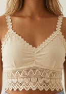 Nahaufnahme des Ayni Ppacha Crop Tops 'Gracia' in Beige. Sichtbar ist die exquisite Textur der ungefärbtem 100% Tanguis-Baumwolle sowie die filigranen, handgearbeiteten Häkel-Träger mit Blüten-Saum. Die architektonische Spitze am Unterbrustband vereint handwerkliche Meisterschaft mit moderner Feminität – perfekt für anspruchsvolle Sommer-Looks.