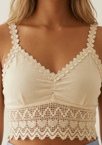 Nahaufnahme des Ayni Ppacha Crop Tops 'Gracia' in Beige. Sichtbar ist die exquisite Textur der ungefärbtem 100% Tanguis-Baumwolle sowie die filigranen, handgearbeiteten Häkel-Träger mit Blüten-Saum. Die architektonische Spitze am Unterbrustband vereint handwerkliche Meisterschaft mit moderner Feminität – perfekt für anspruchsvolle Sommer-Looks.