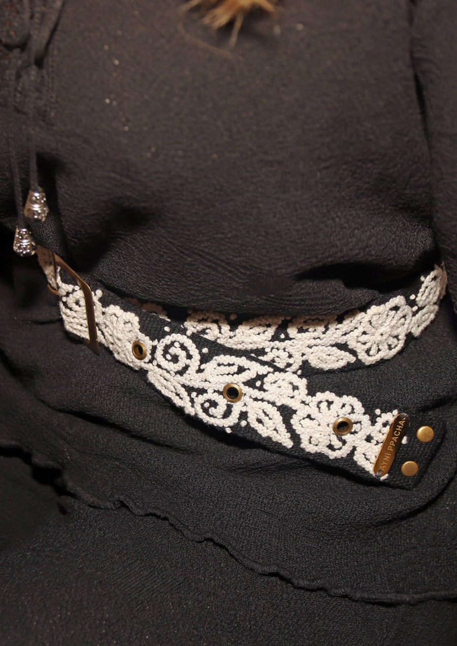 Detailaufnahme der Stickerei und Metallschnalle des handbestickten Ayni Ppacha Gürtels 'Aura' aus 100% Schafwolle, in Schwarz/Weiß.