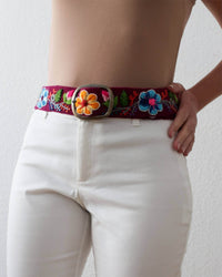 Ayni Ppacha Gürtel Pétalo für Damen, in Peru aus Wolle bestickt mit Blumenmuster auf bordeauxfarbener Basis, stilvoll kombiniert zu einem eleganten Outfit.