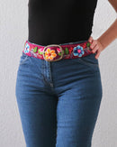 Ayni Ppacha Gürtel Pétalo für Damen, in Peru aus Wolle bestickt mit Blumenmuster auf bordeauxfarbener Basis, stilvoll kombiniert zu einer blauen Jeans.