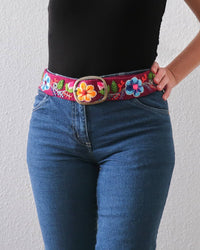 Ayni Ppacha Gürtel Pétalo für Damen, in Peru aus Wolle bestickt mit Blumenmuster auf bordeauxfarbener Basis, stilvoll kombiniert zu einer blauen Jeans.