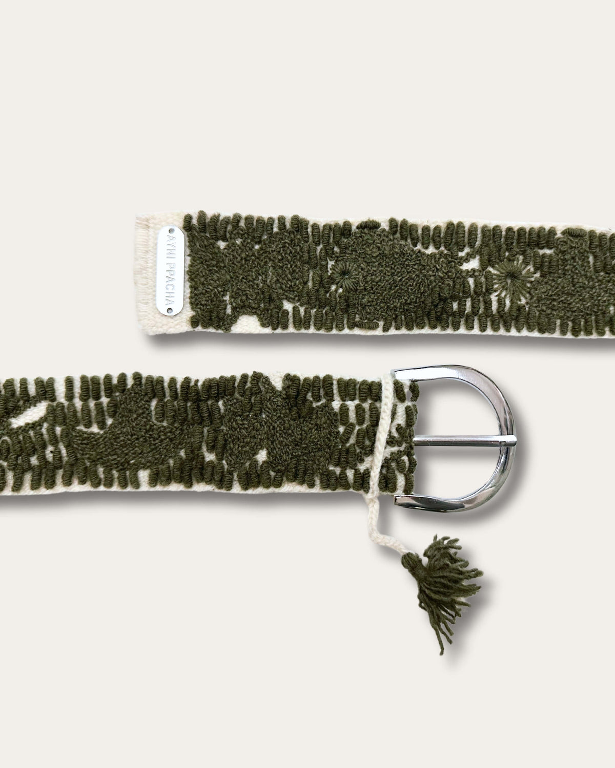 Beide Enden des Gürtels Gírgola: silberfarbene D-Schnalle mit Quaste und Metallplakette mit Schriftzug Ayni Ppacha