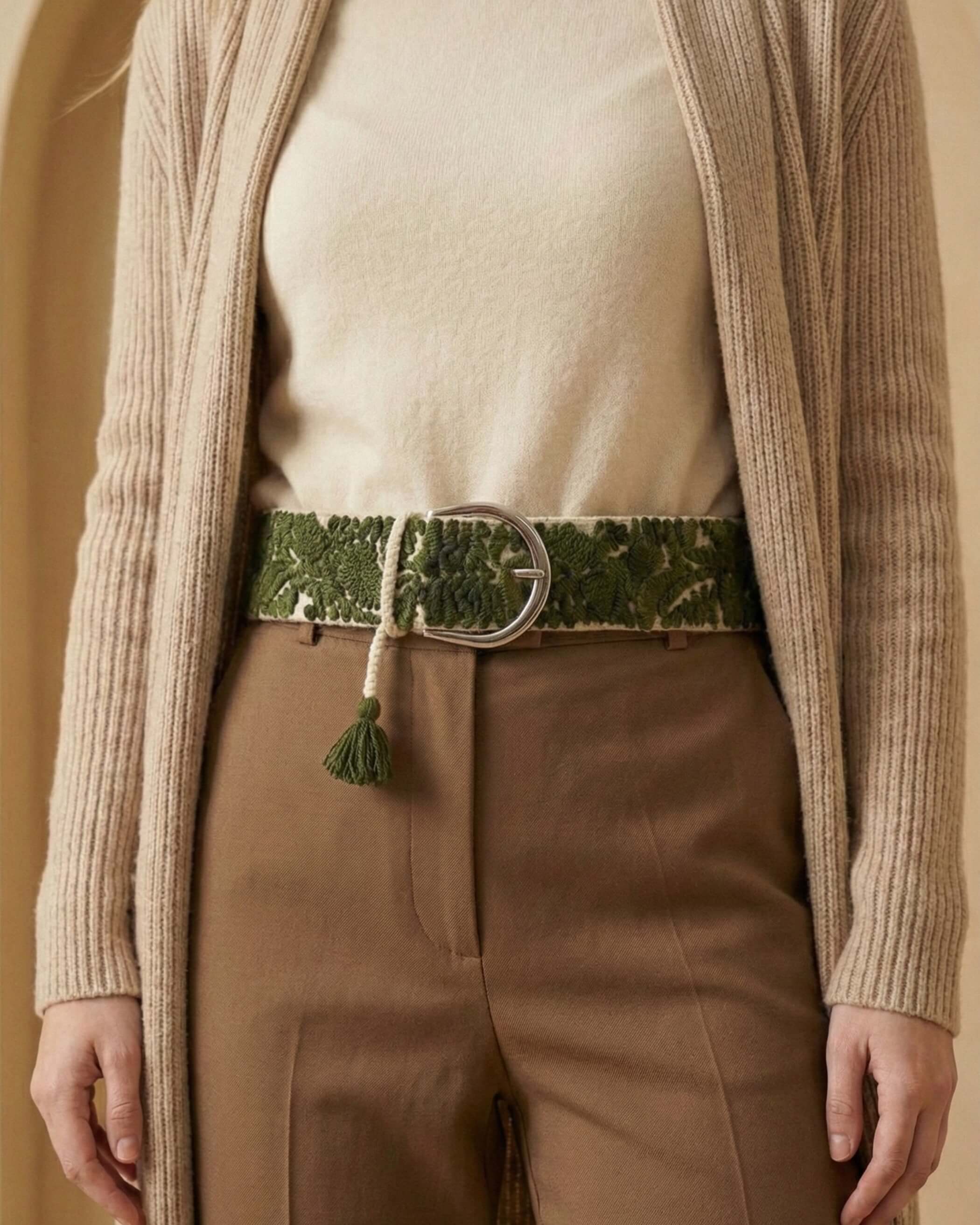 Detailaufnahme des handbestickten Gürtels 'Gírgola' aus 100% natürlich gefärbter Schafwolle, der perfekt durch die Schlaufen einer braunen Hose passt und die grüne kunstvolle Stickerei zeigt.