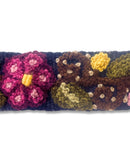 Nahaufnahme der feinen Handstickerei des dunkelblauen Gürtels 'Ilusión', die die Textur der natürlich gefärbten Wolle und die detailreichen bunten Stickmotive in gedeckten Farben zeigt.