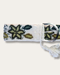 Cinturón Nolina de Ayni Ppacha, primer plano de la hebilla: lana de oveja en blanco natural, bordado a mano con una flor de estrella verde oliva y hojas en tonos verdes, hebilla en D plateada con borla