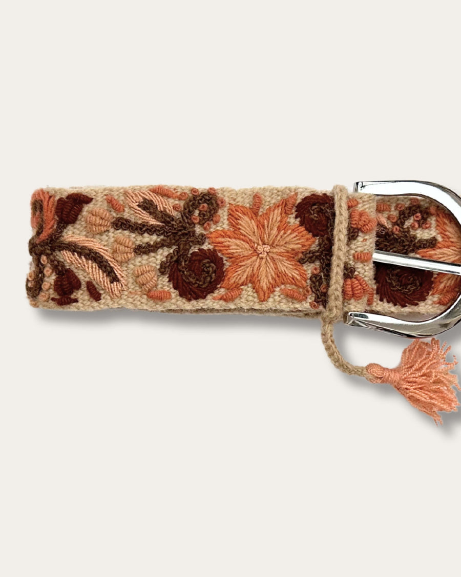 Gürtel Otoño von Ayni Ppacha, Nahaufnahme an der Schnalle: sandfarbene Schafwolle, handbestickt mit Blüten und Ranken in Terrakotta, Apricot und Rotbraun, silberfarbene D-Schnalle mit Quaste