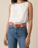 Der handbestickte Gürtel 'Ponsetia' von Ayni Ppacha aus orangener Schafwolle. Das detailreiche florale Muster in Rot, grün und Pink bildet einen lebendigen Kontrast zu Blue Jeans und einem schlichten weißen Top.