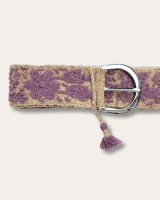 Gürtel Violeta von Ayni Ppacha, Nahaufnahme an der Schnalle: sandfarbene Schafwolle, handbestickt mit Blüten und Ranken in Violett, silberfarbene D-Schnalle mit Quaste