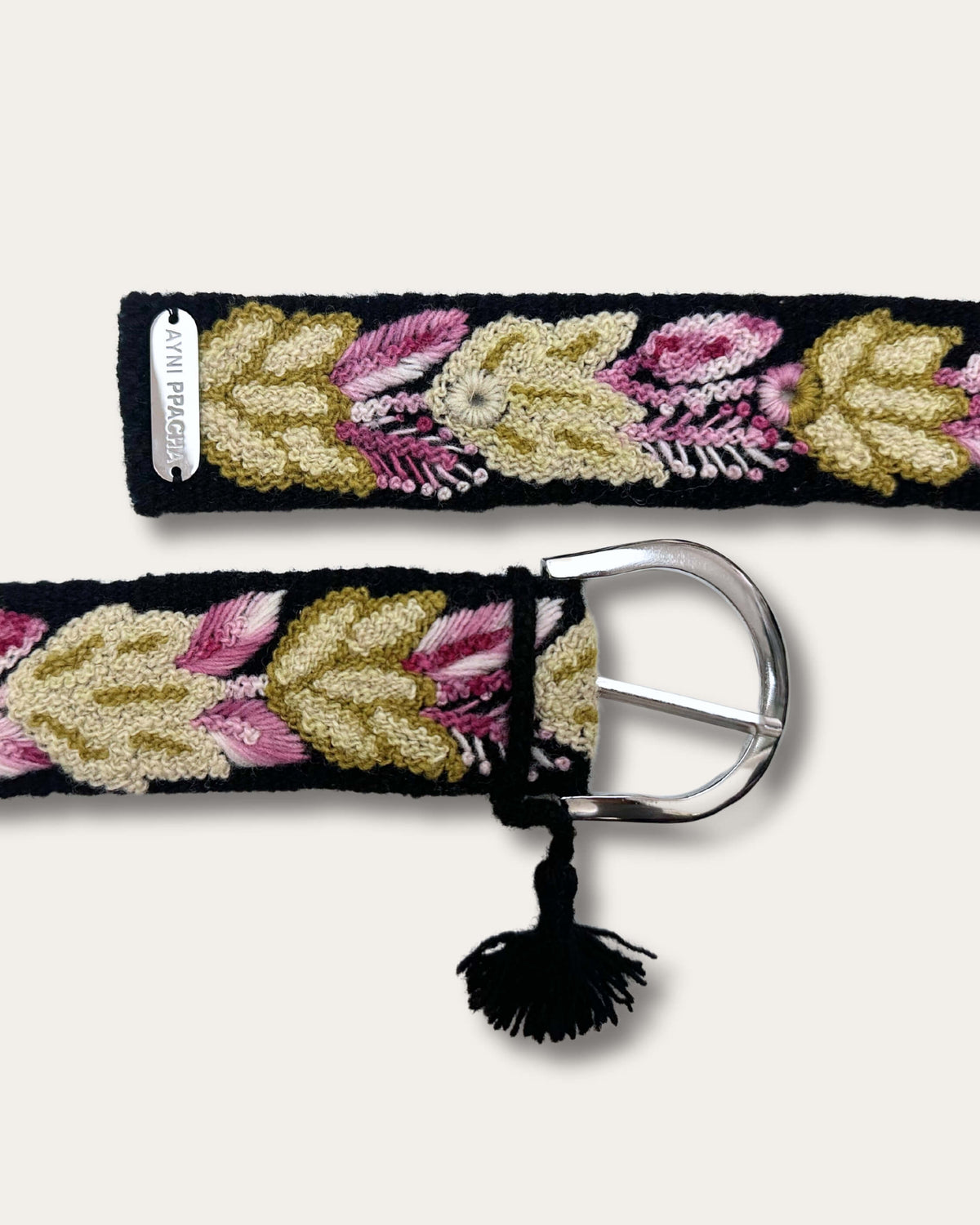 Both ends of the Yagua belt: silver-tone D-buckle with tassel and metal plate with the Ayni Ppacha name