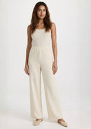 Das Model präsentiert die beige Hose 'Pradera' von Ayni Ppacha. Der High-Waist-Schnitt und das gerade Bein aus strukturiertem Nazca-Baumwollwebstoff erzeugen eine elegante, fließende Silhouette.