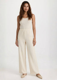 Das Model präsentiert die beige Hose 'Pradera' von Ayni Ppacha. Der High-Waist-Schnitt und das gerade Bein aus strukturiertem Nazca-Baumwollwebstoff erzeugen eine elegante, fließende Silhouette.