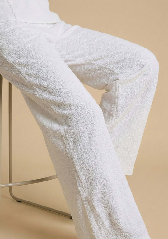Nahaufnahme der weißen Hose 'Pradera' im Sitzen, die die haptische Textur des Nazca-Baumwollstoffs hervorhebt. Der entspannte Relaxed-Fit-Schnitt sorgt für eine fließende Silhouette.