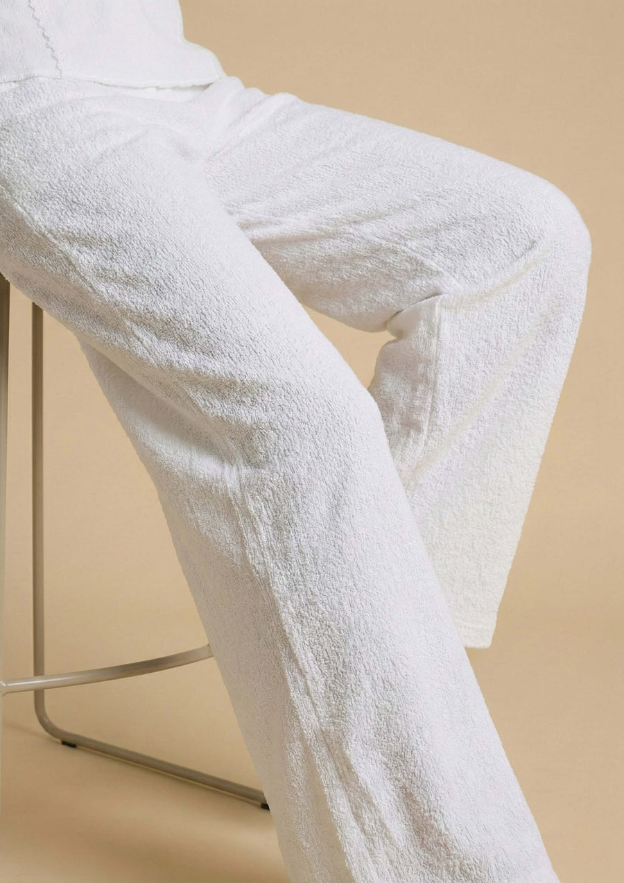 Nahaufnahme der weißen Hose 'Pradera' im Sitzen, die die haptische Textur des Nazca-Baumwollstoffs hervorhebt. Der entspannte Relaxed-Fit-Schnitt sorgt für eine fließende Silhouette.