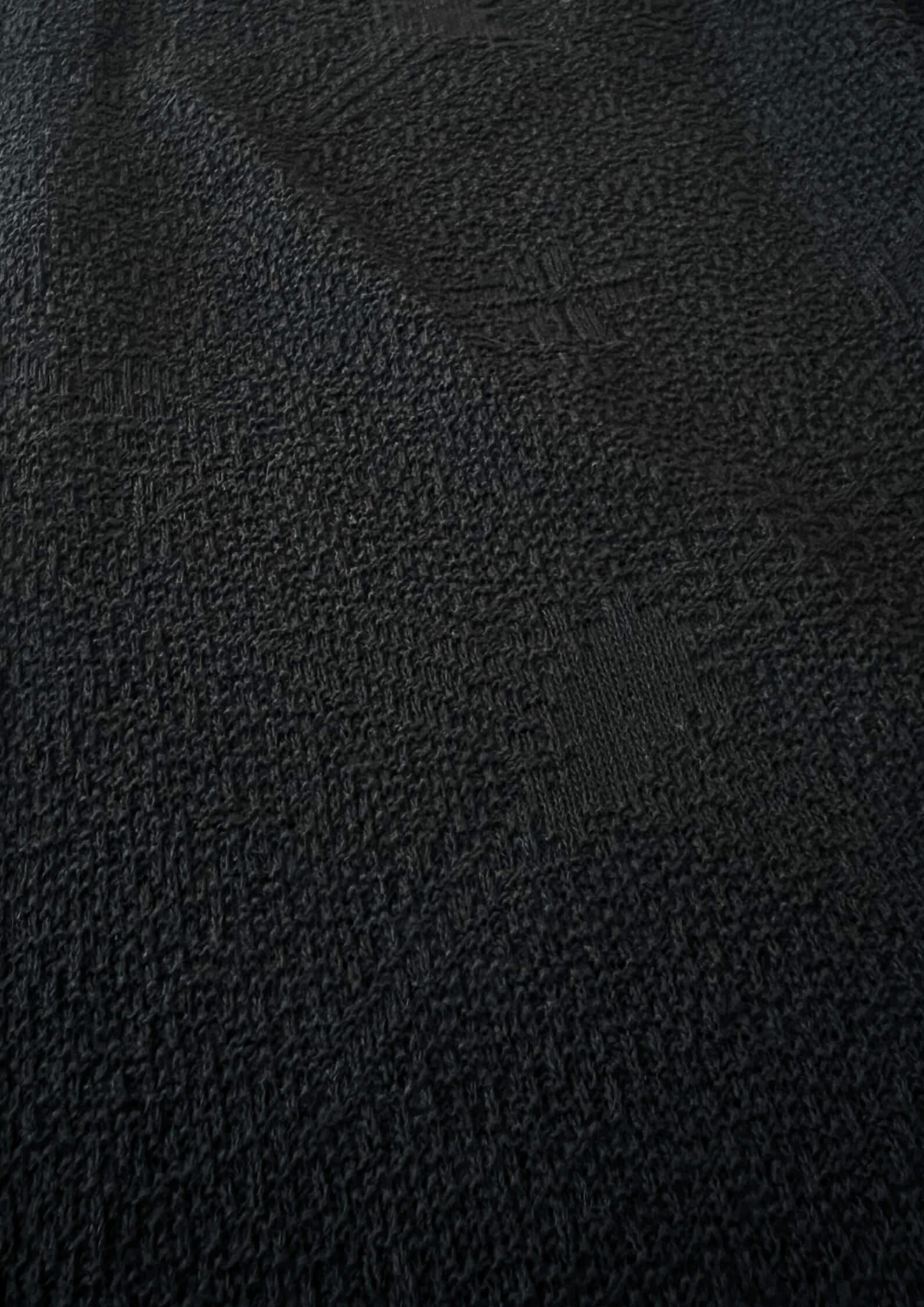 Makro-Nahaufnahme der schwarzen, strukturierten Nazca-Baumwolltextur von Ayni Ppacha. Der grobe, reliefartig gewebte Stoff zeigt eingewebte geometrische Symbole und Muster. Die haptische Oberfläche vermittelt ein authentisches, handwerkliches Gefühl der natürlichen peruanischen Faser und zeigt die Materialtiefe.
