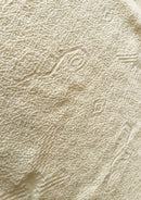 Makro-Nahaufnahme der ungefärbten, sandbeigen Baumwolltextur von Ayni Ppacha. Der grobe aber zugleich weiche, strukturiert gewebte Stoff zeigt reliefartige, eingewebte Nazca-Symbole und geometrische Muster. Die Aufnahme vermittelt ein authentisches, handwerkliches Gefühl der natürlichen peruanischen Faser.