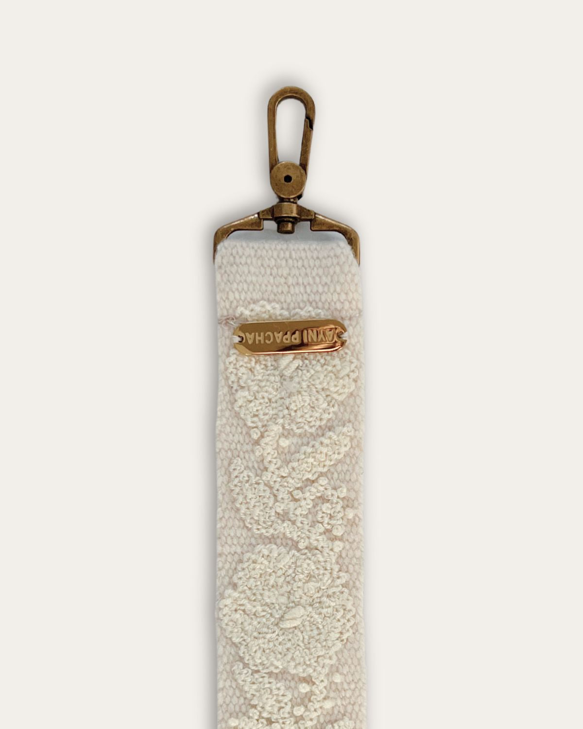 End of the Coco bag strap by Ayni Ppacha with brass-tone carabiner and engraved logo plate, natural white sheep wool with tone-on-tone hand embroidery