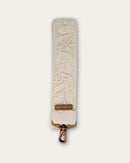 Section of the Coco bag strap by Ayni Ppacha: tone-on-tone floral tendrils on natural white sheep wool, with logo plate and brass-tone carabiner below