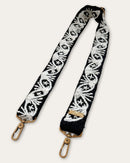 Lodoño bag strap by Ayni Ppacha laid out diagonally: black sheep wool with natural white hand embroidery of medallions and fan motifs, two brass-tone carabiners