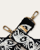 Close-up of the Lodoño bag strap by Ayni Ppacha: star flowers and fan motifs in natural white on black sheep wool, brass-tone carabiner and plate engraved with Ayni Ppacha