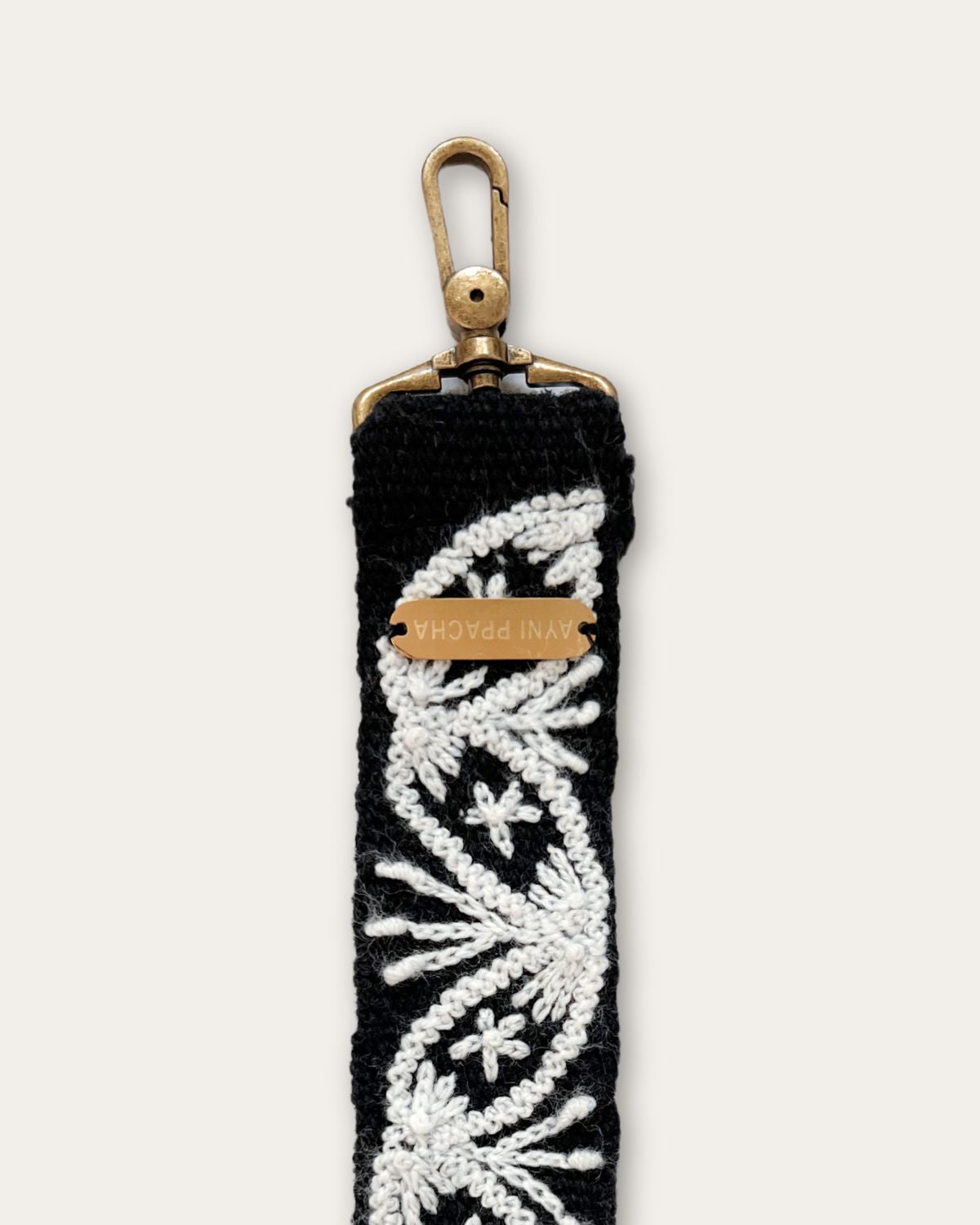 End of the Lodoño bag strap by Ayni Ppacha with brass-tone carabiner and engraved logo plate, black sheep wool with natural white hand embroidery