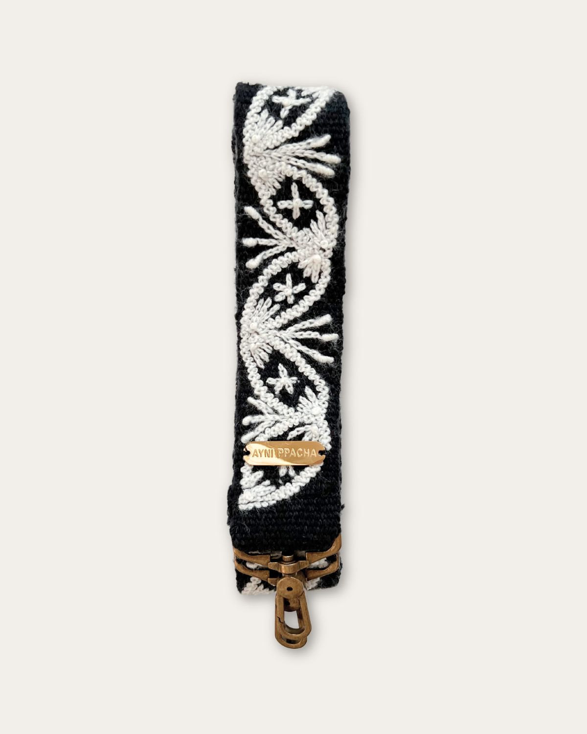 Section of the Lodoño bag strap by Ayni Ppacha: natural white medallion with star flower on black sheep wool, with logo plate and brass-tone carabiner below
