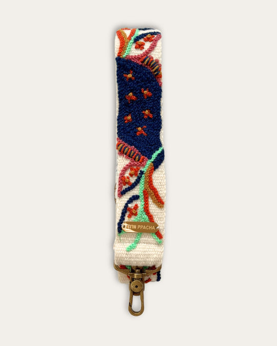 Ausschnitt des Taschengurts Piri Piri von Ayni Ppacha: marineblaue Blattform mit Rostpunkten und mintgrüne Ranke auf naturweißer Schafwolle, darunter Logoplakette und messingfarbener Karabiner