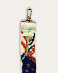 Riemenende des Taschengurts Piri Piri von Ayni Ppacha mit messingfarbenem Karabiner und gravierter Logoplakette, Ranken in Mint und Rost auf naturweißer Schafwolle