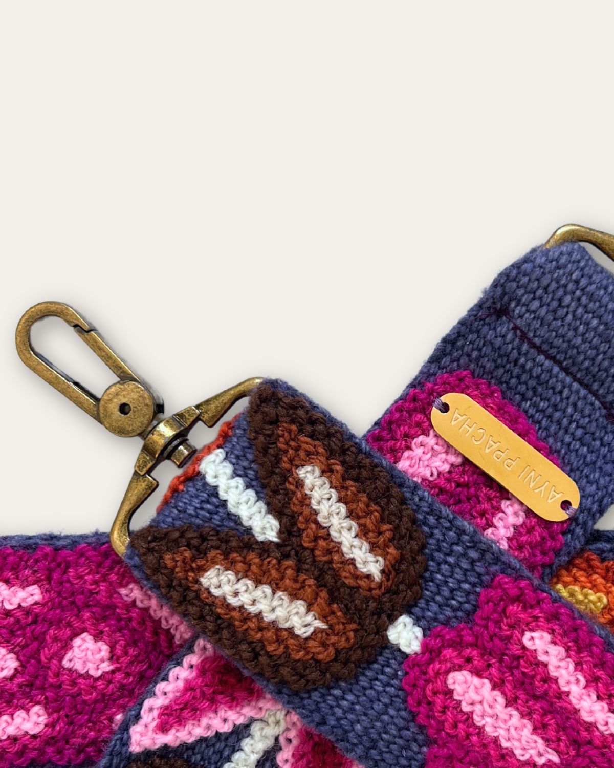 Nahaufnahme des Taschengurts Tulipán von Ayni Ppacha: Tulpen in Braun und Magenta, Stich für Stich auf blauer Schafwolle, messingfarbener Karabiner und Plakette mit Ayni-Ppacha-Gravur
