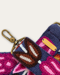 Nahaufnahme des Taschengurts Tulipán von Ayni Ppacha: Tulpen in Braun und Magenta, Stich für Stich auf blauer Schafwolle, messingfarbener Karabiner und Plakette mit Ayni-Ppacha-Gravur