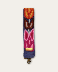 Ausschnitt des Taschengurts Tulipán von Ayni Ppacha: Tulpen in Orange, Braun und Pink auf blauer Schafwolle, darunter Logoplakette und messingfarbener Karabiner
