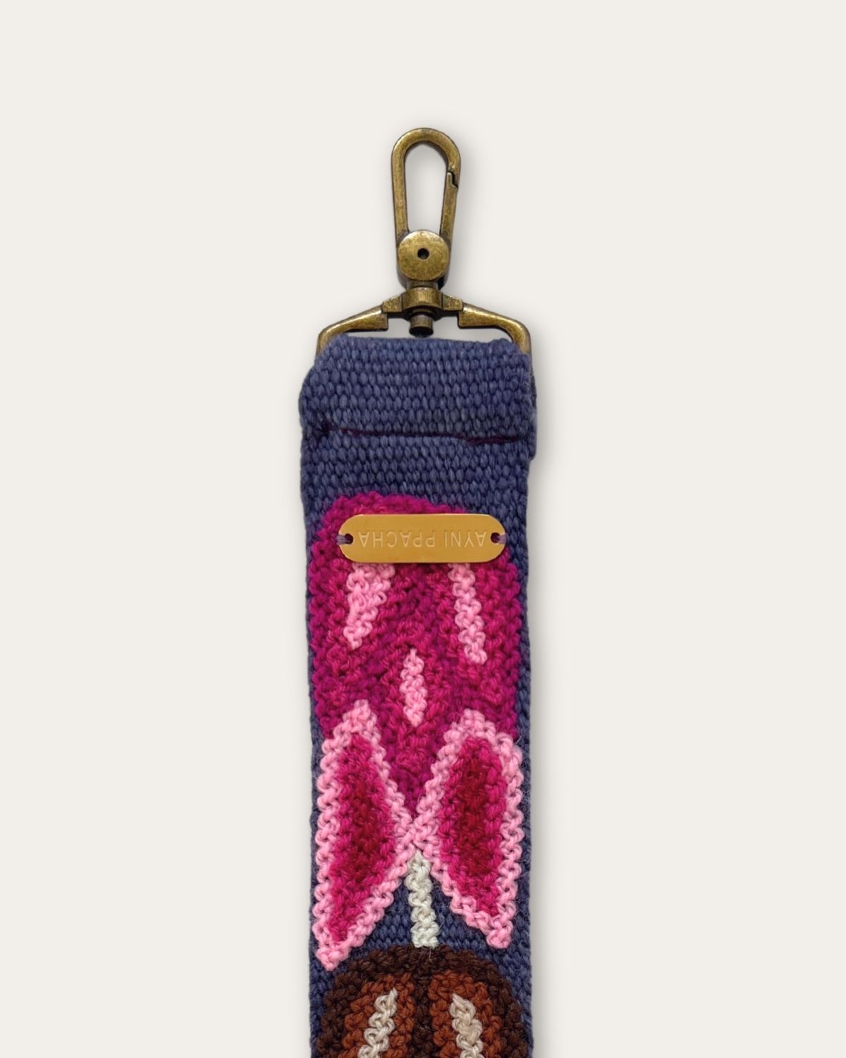 Riemenende des Taschengurts Tulipán von Ayni Ppacha mit messingfarbenem Karabiner und gravierter Logoplakette, Tulpe in Pink und Magenta auf blauer Schafwolle