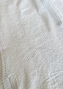 Makro-Ansicht des weißen Tops 'Baila' von Ayni Ppacha. Die architektonische Textur des Nazca-Webstoffs wird durch Häkeldetails (Crochet) ergänzt, die den puristischen Look veredeln.