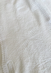 Makro-Ansicht des weißen Tops 'Baila' von Ayni Ppacha. Die architektonische Textur des Nazca-Webstoffs wird durch Häkeldetails (Crochet) ergänzt, die den puristischen Look veredeln.